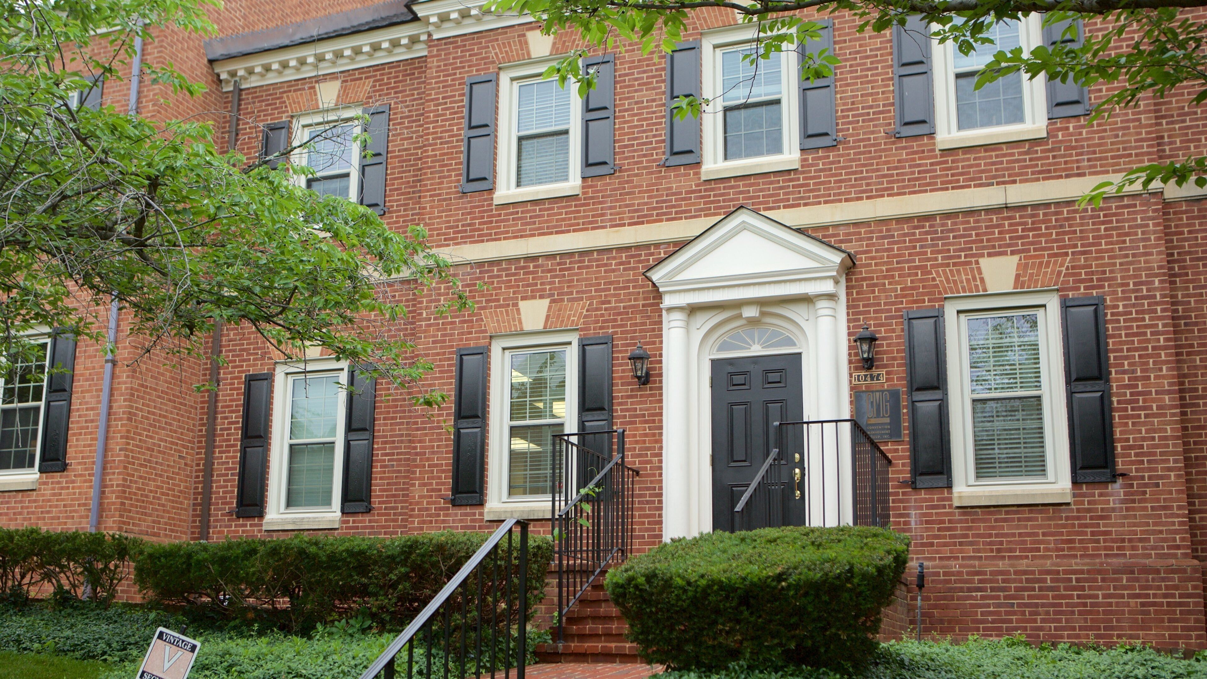 A two-story brick building with black shutters, a white door, and a small front porch.