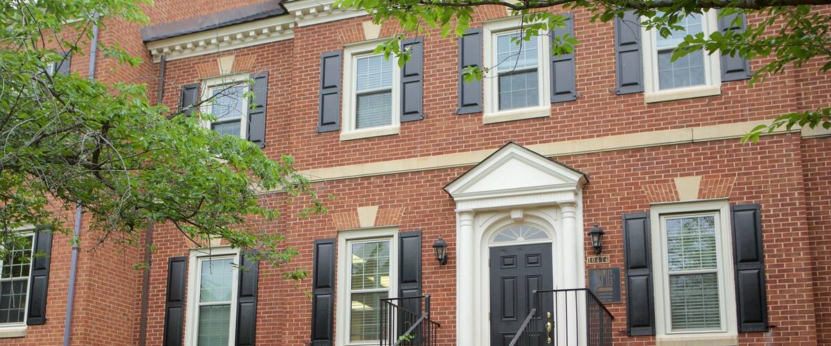 A two-story brick building with black shutters, a white door, and a small front porch.