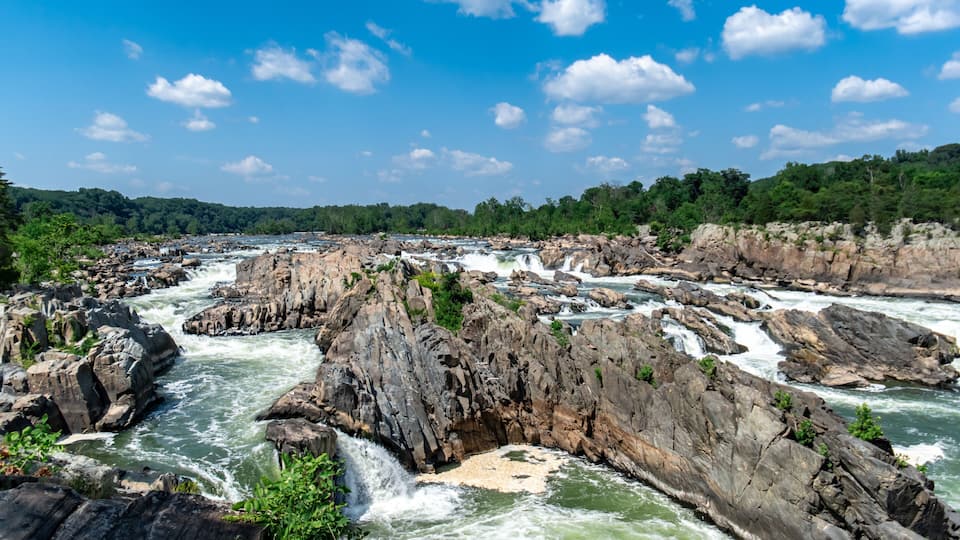 A river with multiple rapids and waterfalls, surrounded by rocky terrain and dense greenery.