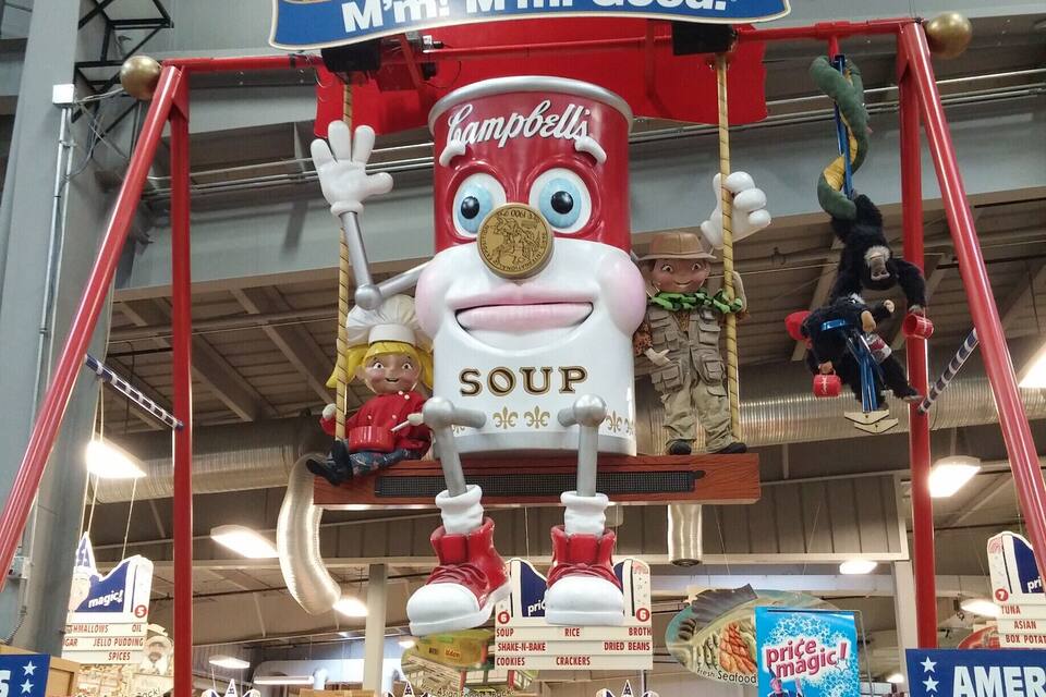 Campbell's Suppe-maskot hænger fra en rød konstruktion i en butik.