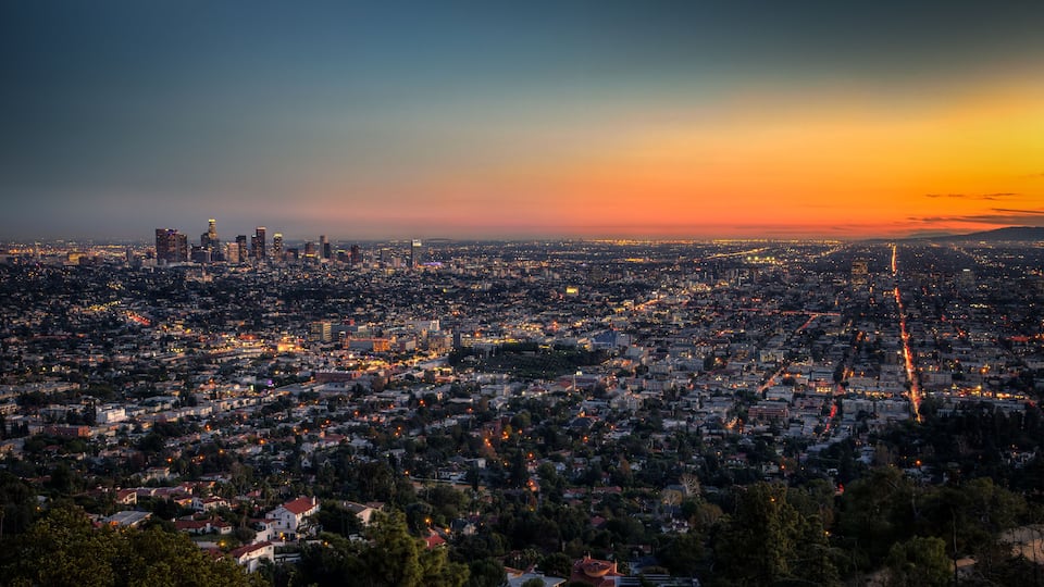 A cityscape at dusk with a prominent skyline, dense residential areas, and a visible highway.