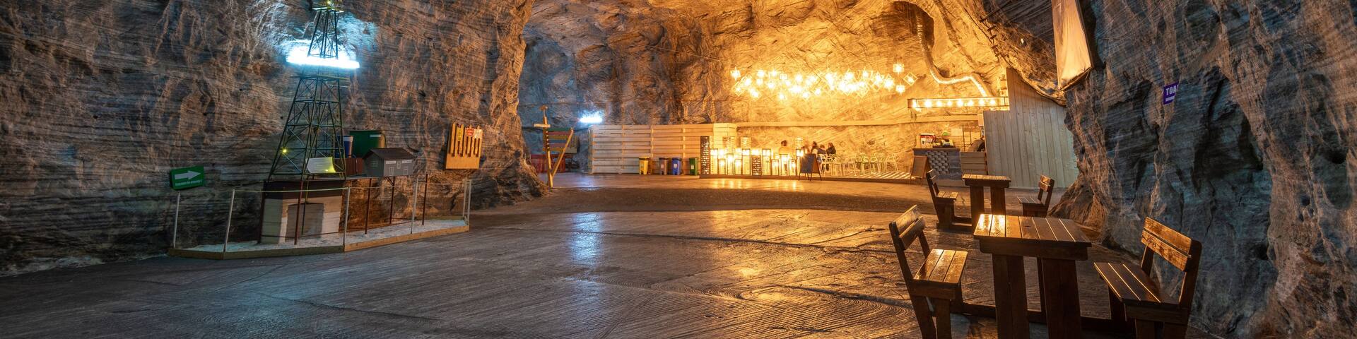 An underground cavern with wooden benches and tables, illuminated by artificial lighting.