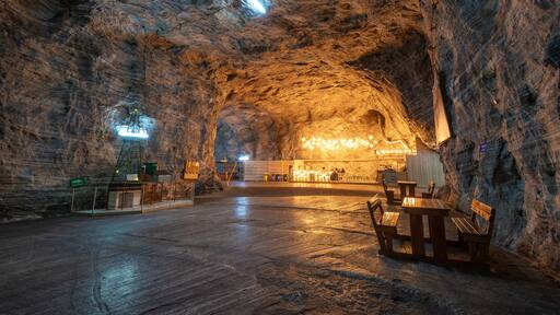 An underground cavern with wooden benches and tables, illuminated by artificial lighting.