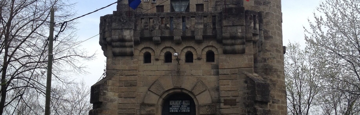 Um edifício histórico de pedra com cúpula e janelas em arco, exibindo bandeiras e uma placa.