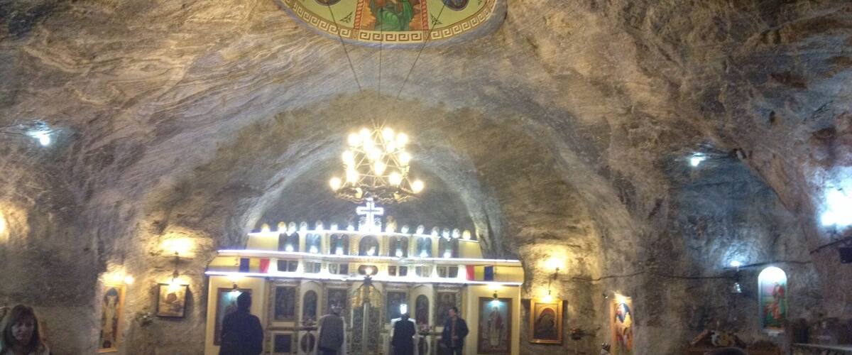An interior of a cave church with a central altar, chandeliers, and religious paintings.