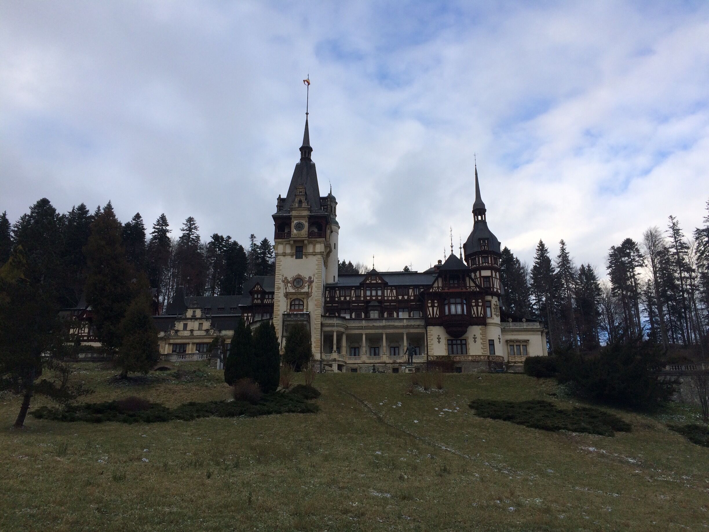 A historic building with two towers and a clock tower, surrounded by trees and a grassy area.