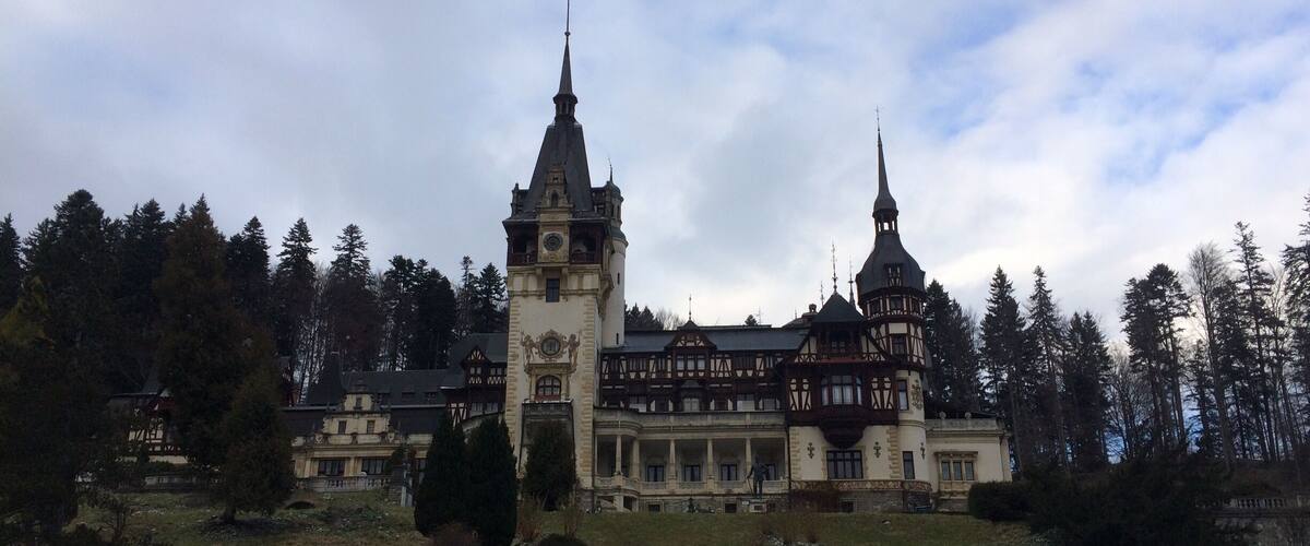 A historic building with two towers and a clock tower, surrounded by trees and a grassy area.