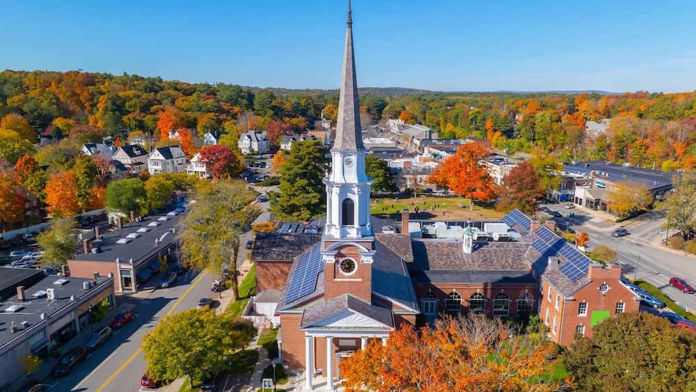 A church with a tall steeple, surrounded by autumn-colored trees and residential buildings.
