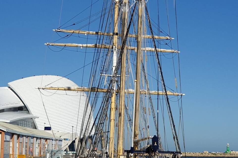 A tall ship docked at a pier with a clear blue sky.