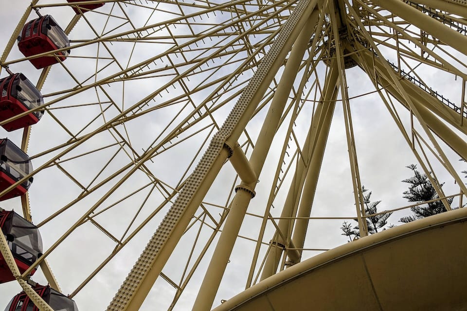 A large Ferris wheel with red cabins, set against a cloudy sky.