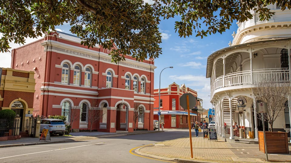 A street with historic buildings, including a red brick building labeled 'Trades Hall' and a white building with a balcony.