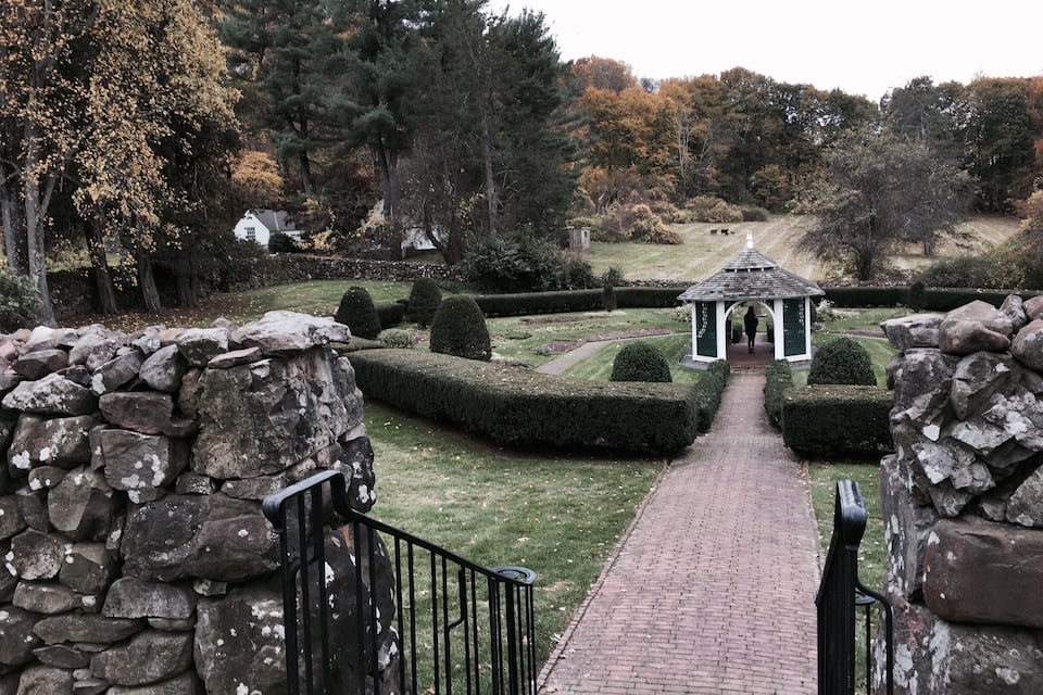A stone pathway leading to a gazebo in a landscaped garden with trimmed hedges and trees.