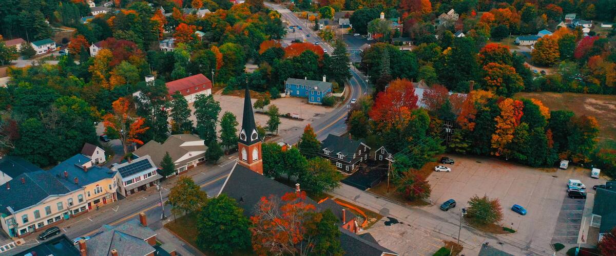 Una vista aerea di una città con alberi dai colori dell'autunno, una chiesa e edifici residenziali.