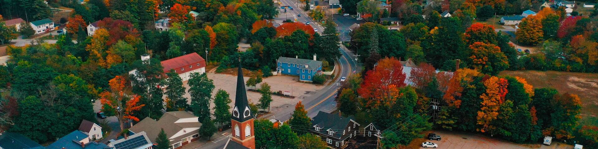 An aerial view of a town with autumn foliage, a church, and residential buildings.