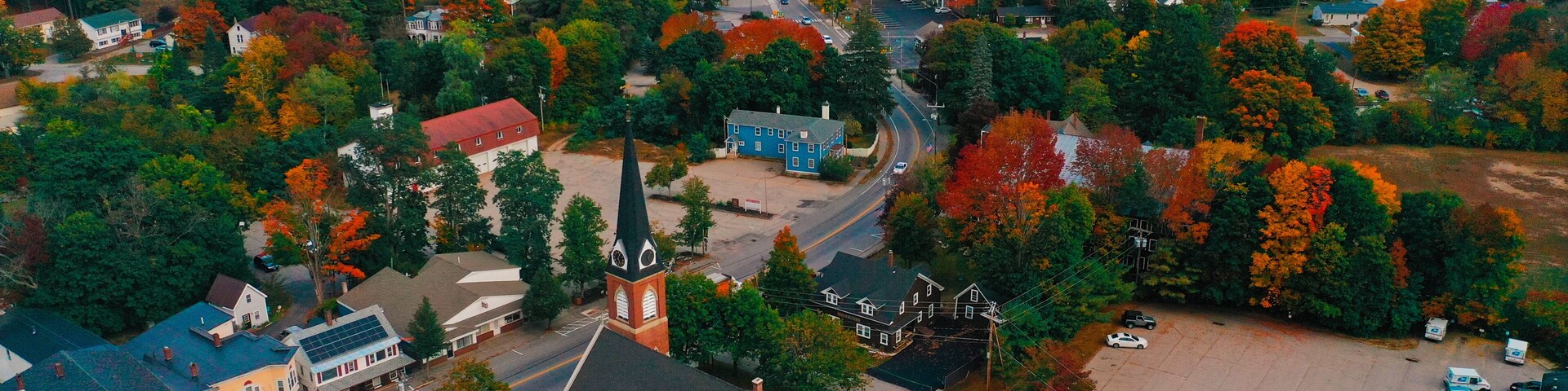 An aerial view of a town with autumn foliage, a church, and residential buildings.