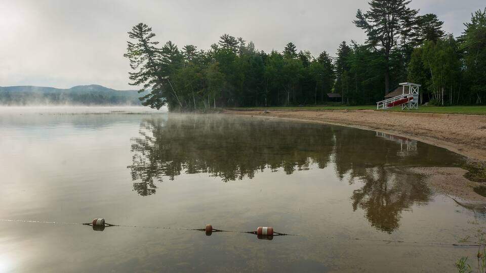 A calm lake with a wooden dock and a lifeguard tower.
