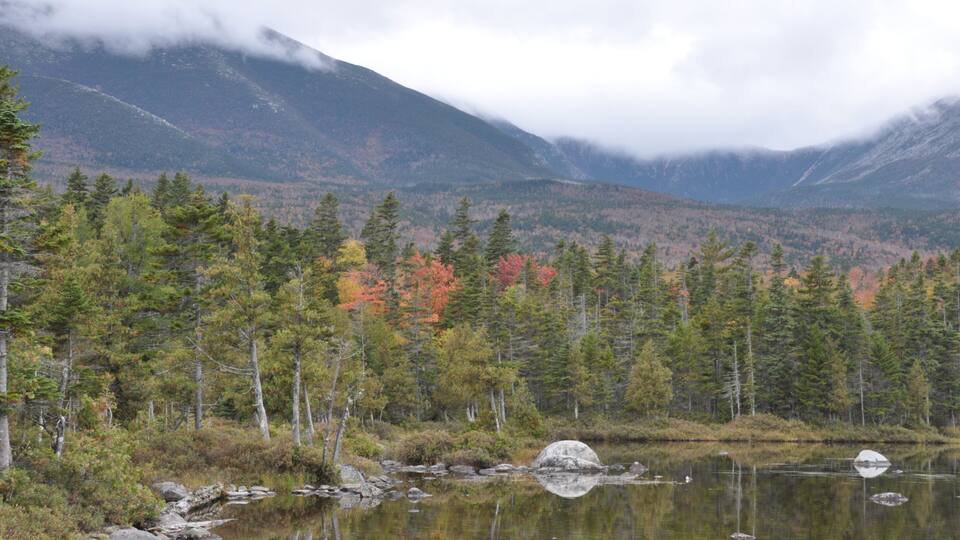 A lake surrounded by autumn-colored trees and mountains in the background.
