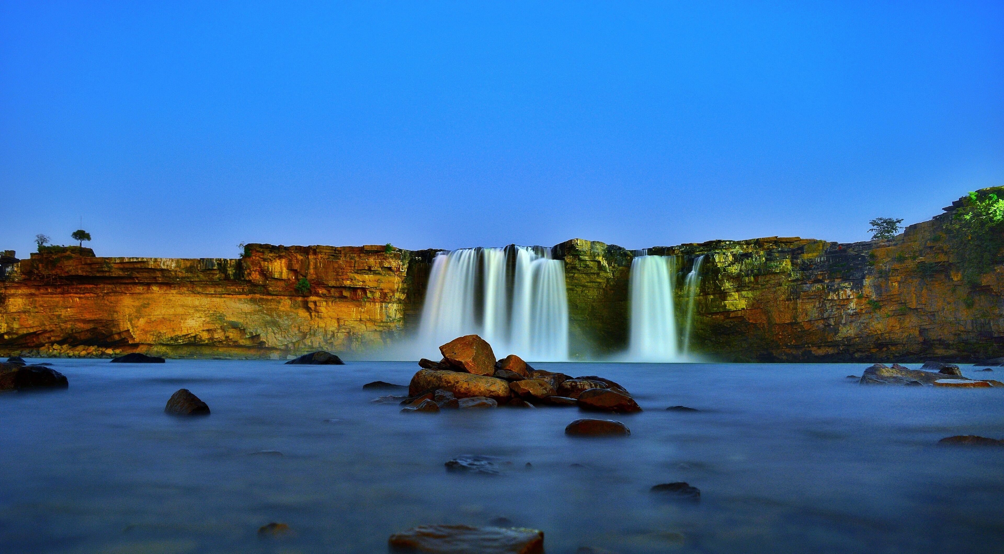 A waterfall cascading over a cliff into a river surrounded by rocks.