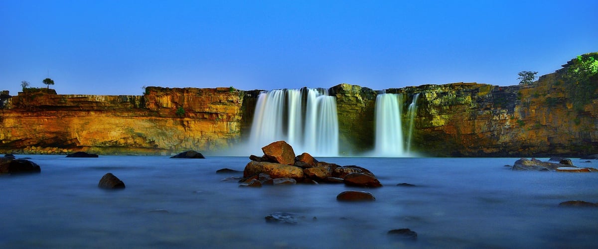 A waterfall cascading over a cliff into a river surrounded by rocks.