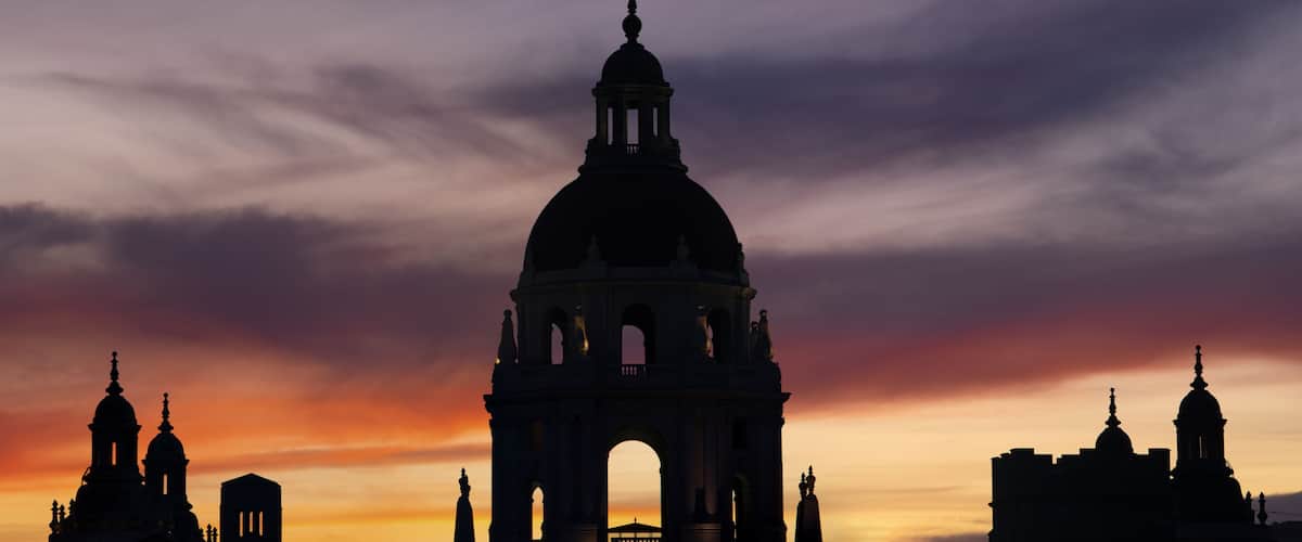 A grand architectural structure with a dome and arches, silhouetted against a sunset sky.