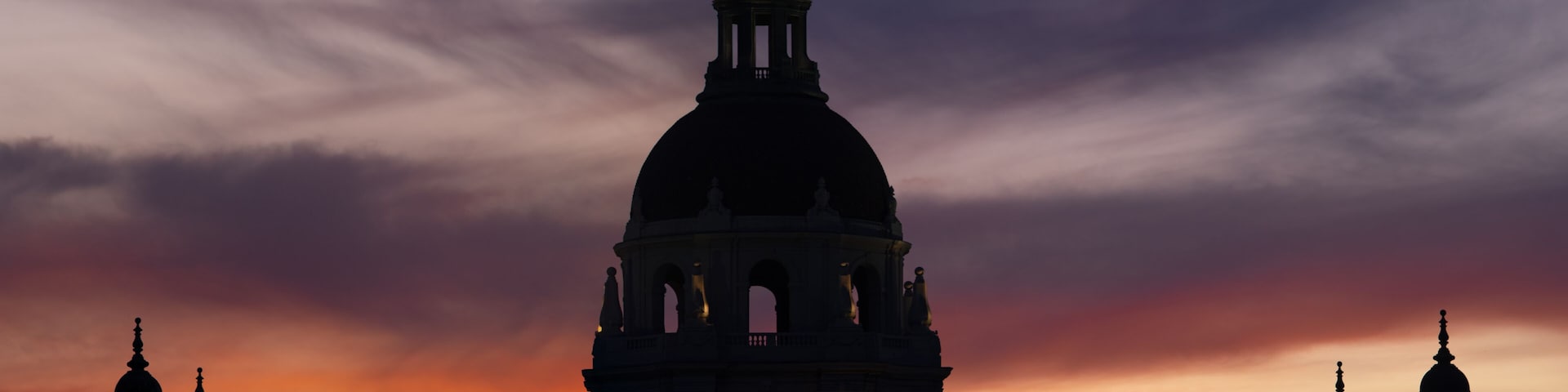 A grand architectural structure with a dome and arches, silhouetted against a sunset sky.