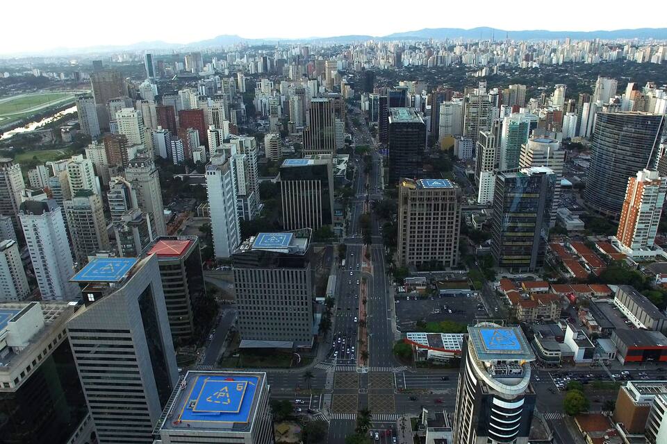 Zona urbana densamente poblada con numerosos edificios altos, un campo deportivo destacado y una vista despejada de las montañas circundantes.