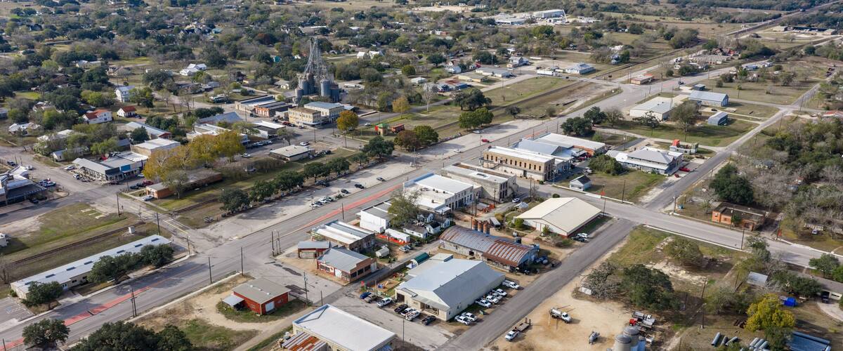 An aerial view of a small town with a mix of residential and industrial buildings, roads, and a railroad track.