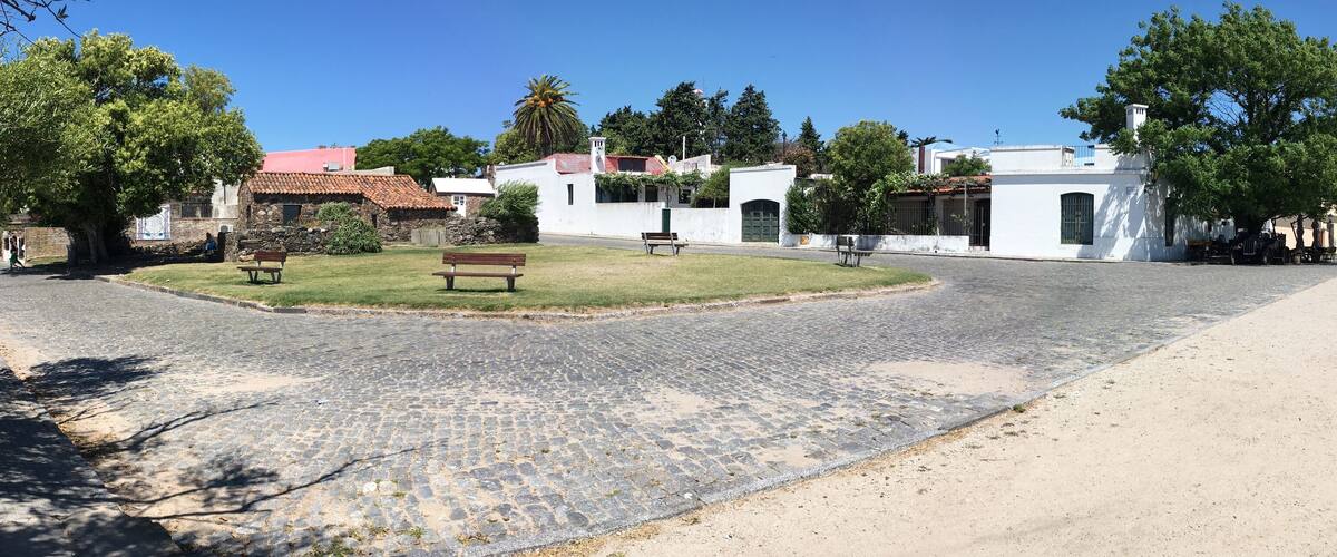 A cobblestone street with benches, white buildings, and trees.