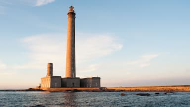 A tall lighthouse on a rocky shore with calm water.