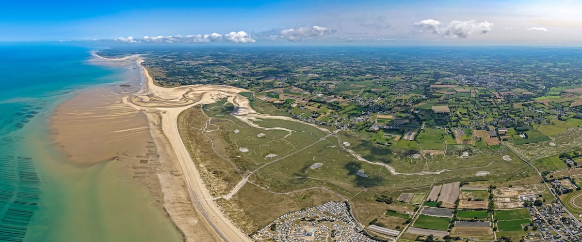 An aerial view of a coastal area with a beach, a river, and a town with fields and buildings.