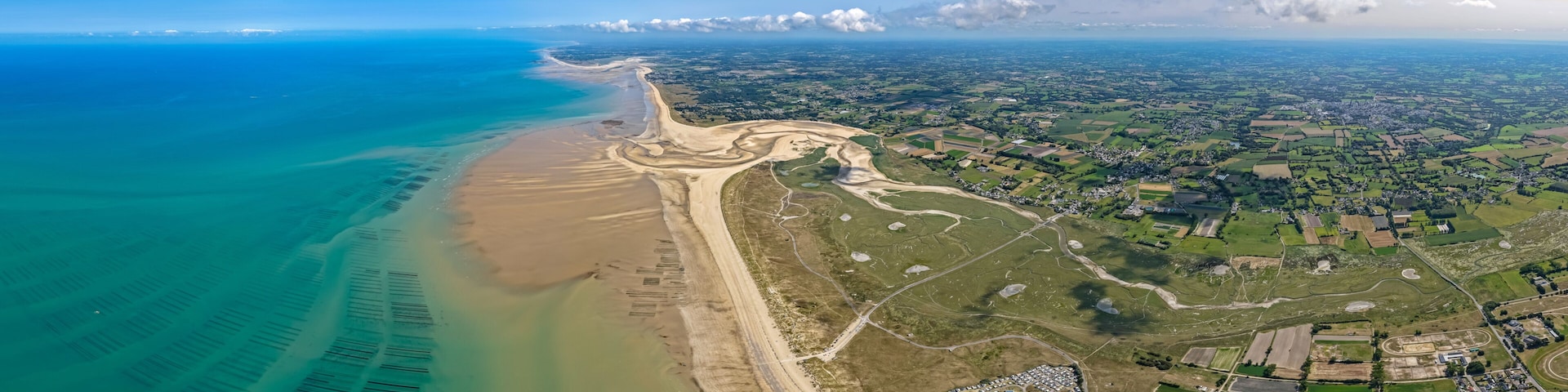 An aerial view of a coastal area with a beach, a river, and a town with fields and buildings.