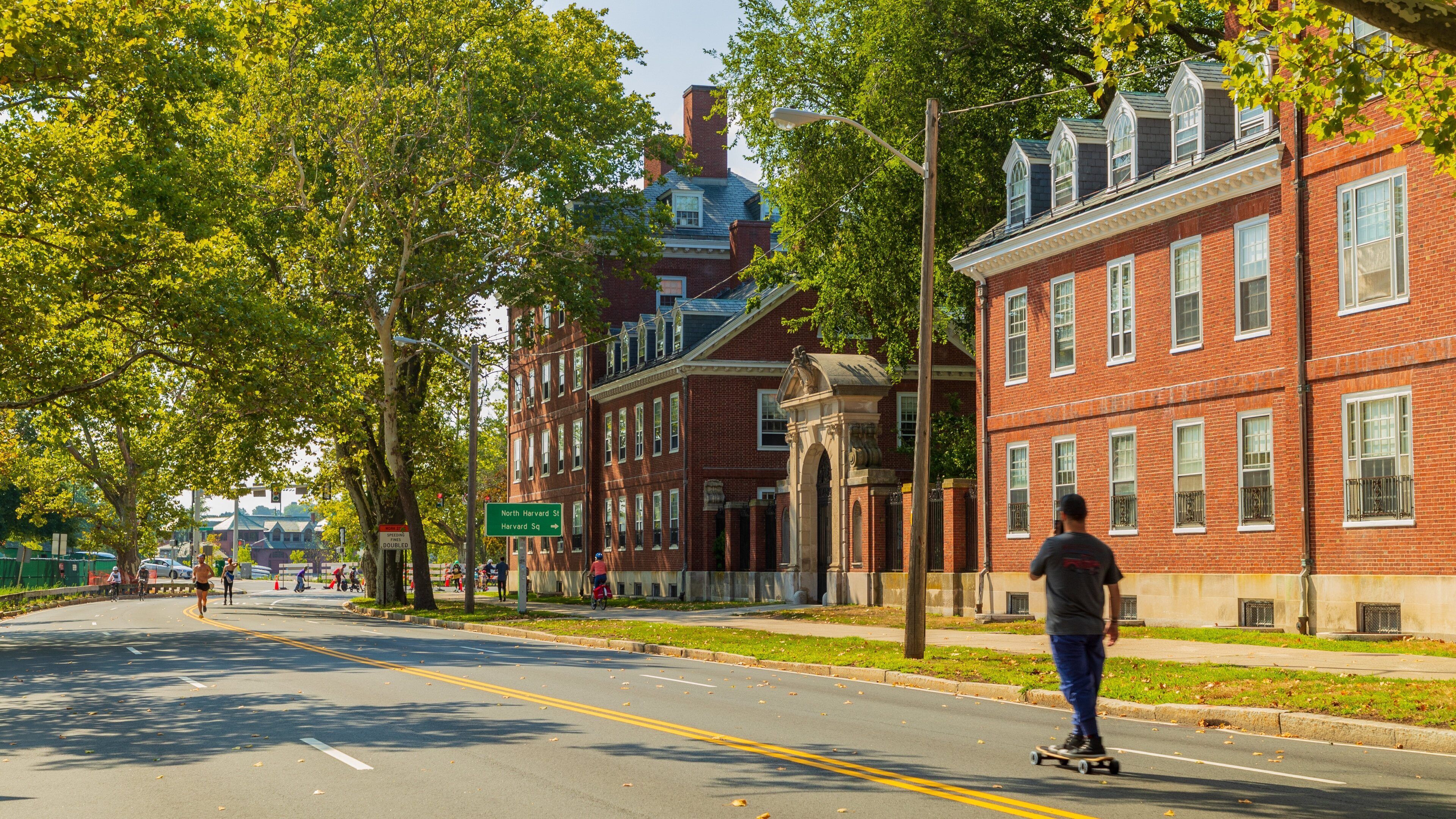 A street lined with red brick buildings, a person skateboarding, and a street sign for North Harvard St.