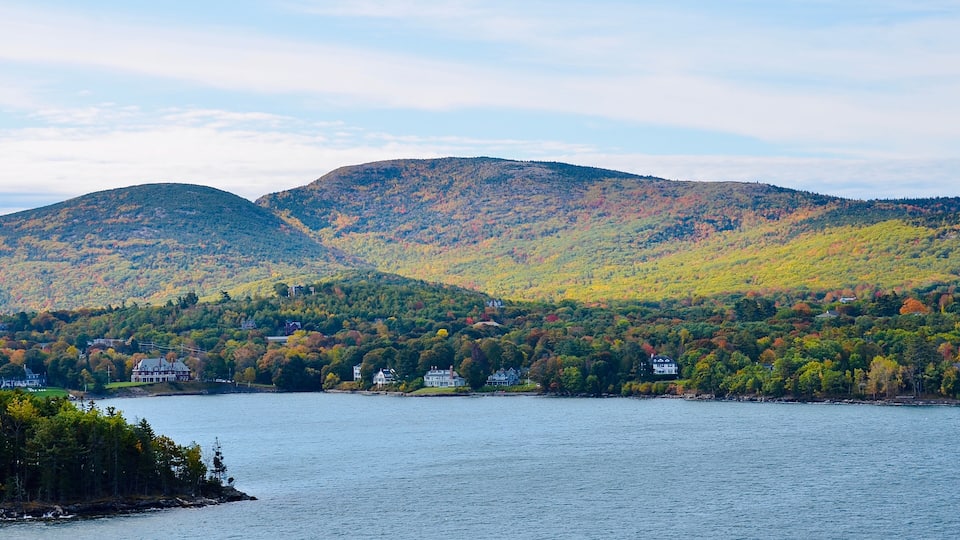 A lake surrounded by hills with autumn foliage, houses along the shore, and a clear sky.