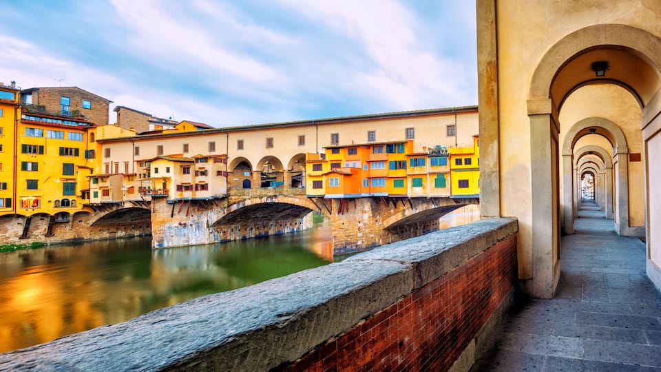 A canal with colorful buildings, a stone bridge, and an arched walkway.