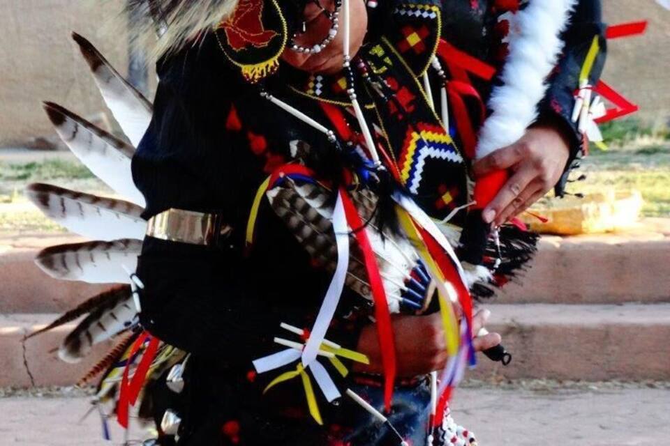 Une personne vêtue d’un costume traditionnel amérindien, portant un couvre-chef orné de plumes et des accessoires décorés de perles.