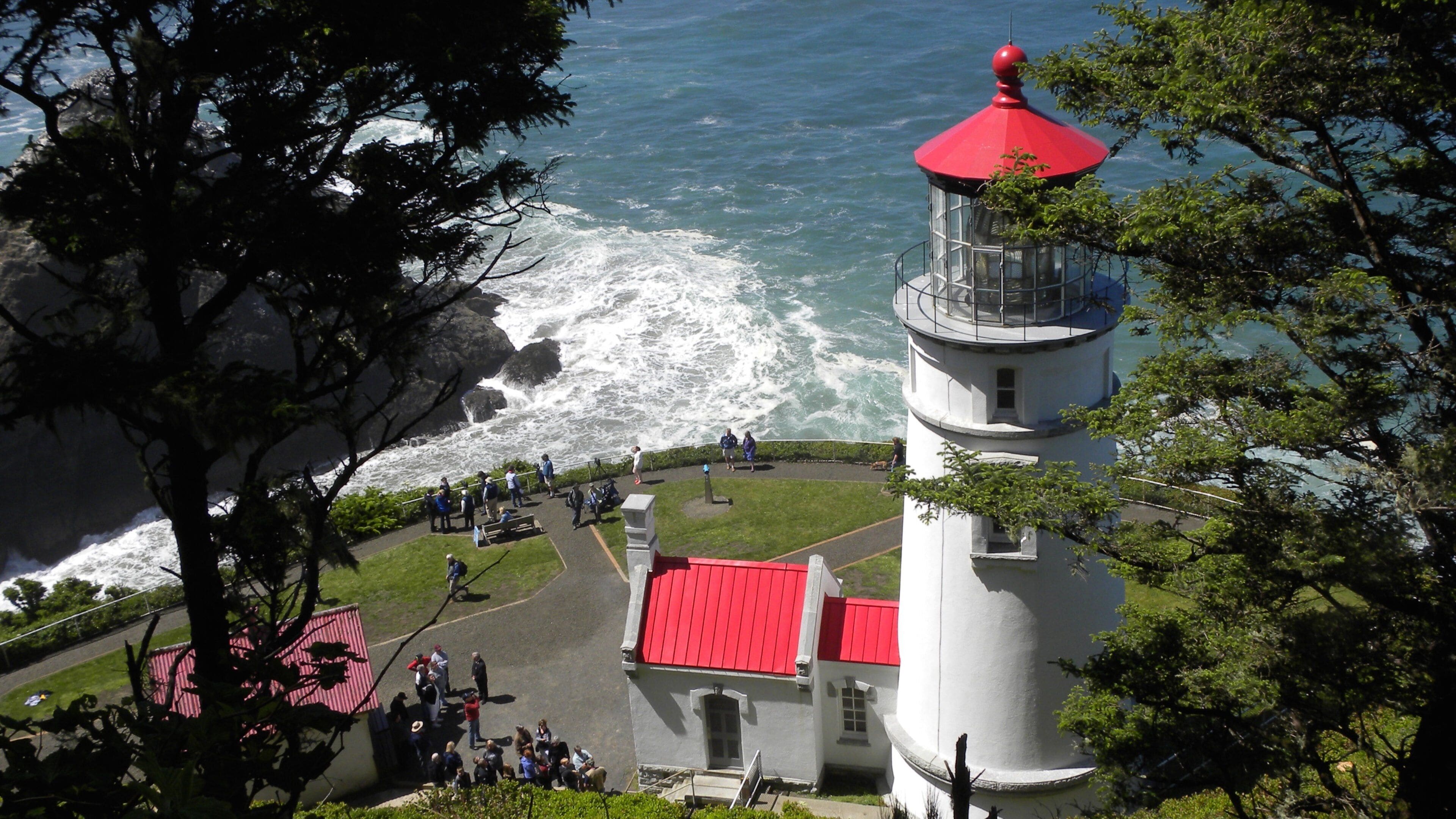A lighthouse with a red roof and a white tower by the ocean.