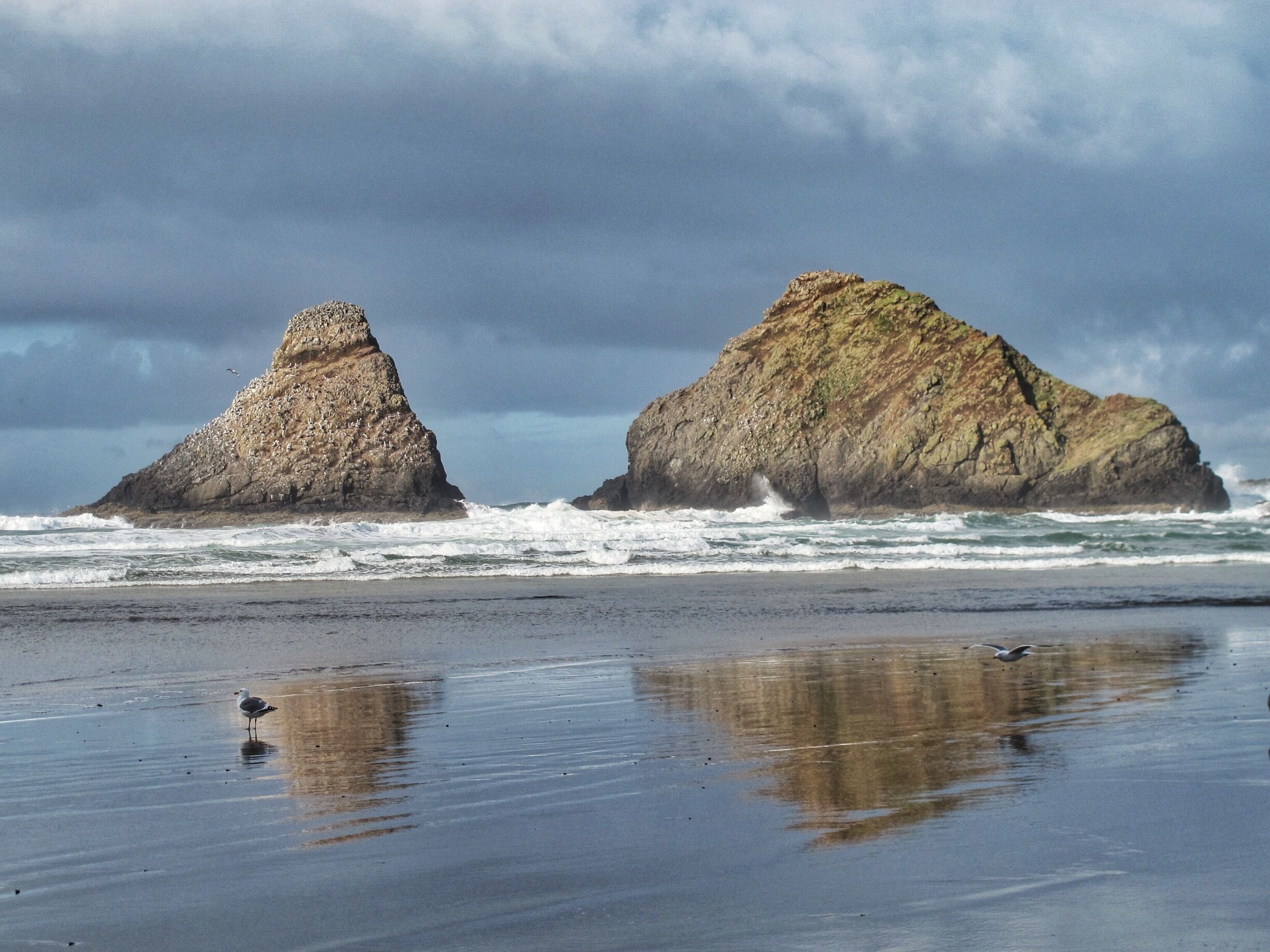 Two rocky formations on a beach with waves crashing against them.