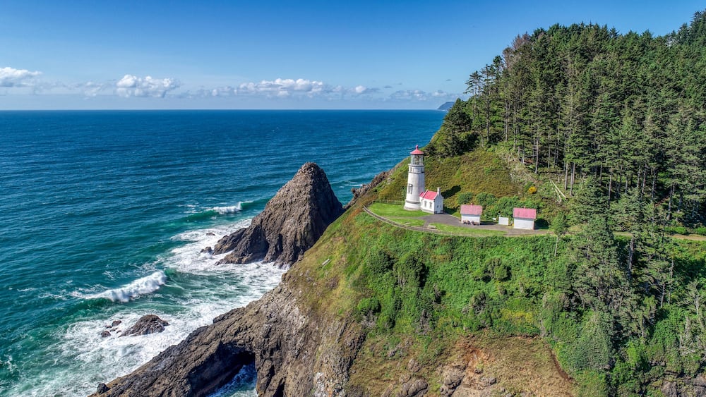 A coastal landscape with a lighthouse and buildings on a cliff overlooking the ocean.