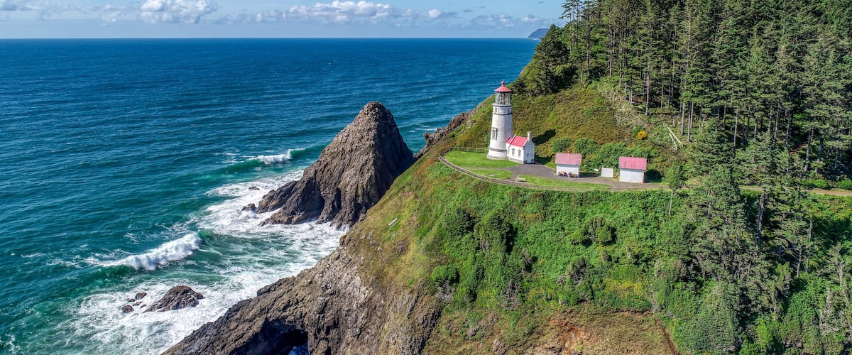 A coastal landscape with a lighthouse and buildings on a cliff overlooking the ocean.