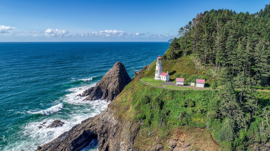 A coastal landscape with a lighthouse and buildings on a cliff overlooking the ocean.