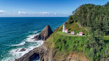 A coastal landscape with a lighthouse and buildings on a cliff overlooking the ocean.