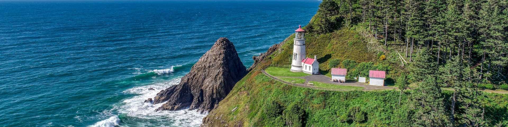 Un paisaje costero con un faro y edificios sobre un acantilado con vista al océano.