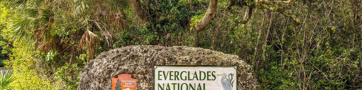 Un panneau indiquant l’entrée du parc national des Everglades, placé sur un grand rocher, avec la végétation environnante.