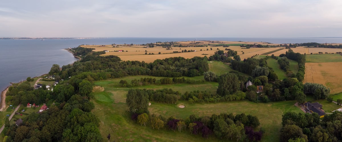 An aerial view of a coastal landscape with fields, trees, and a body of water.