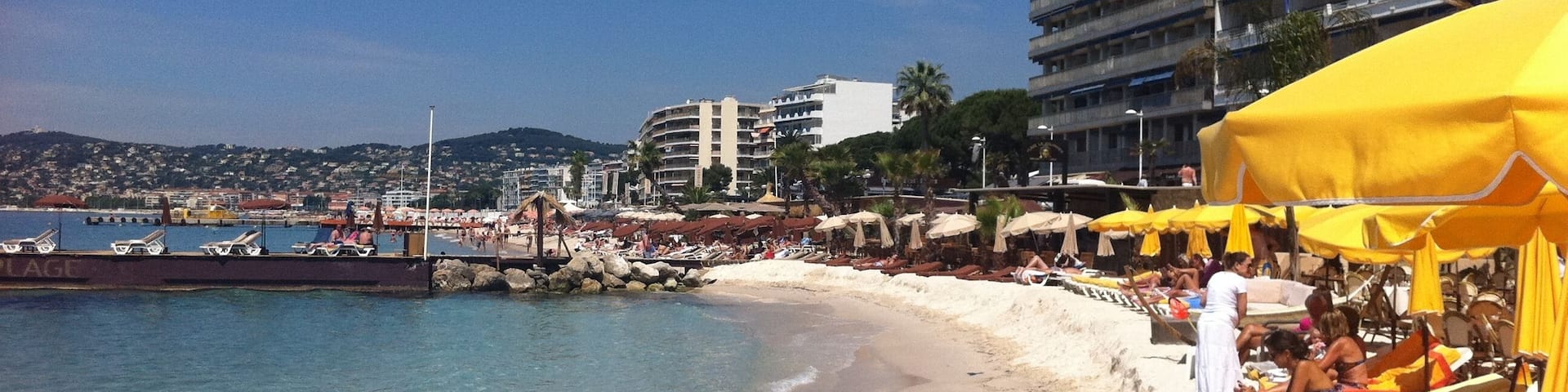 A beach with yellow umbrellas and lounge chairs, a pier, and buildings in the background.