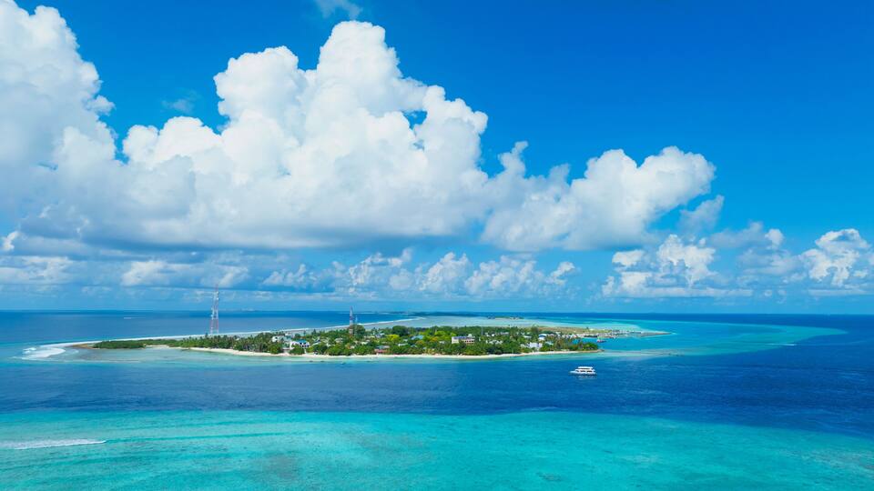 A tropical island with clear turquoise waters, a small boat, and a lighthouse.