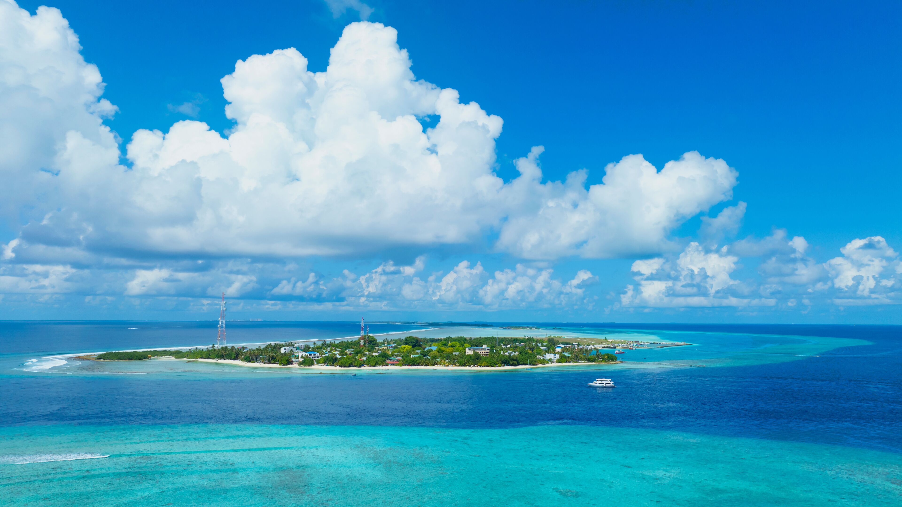A tropical island with clear turquoise waters, a small boat, and a lighthouse.