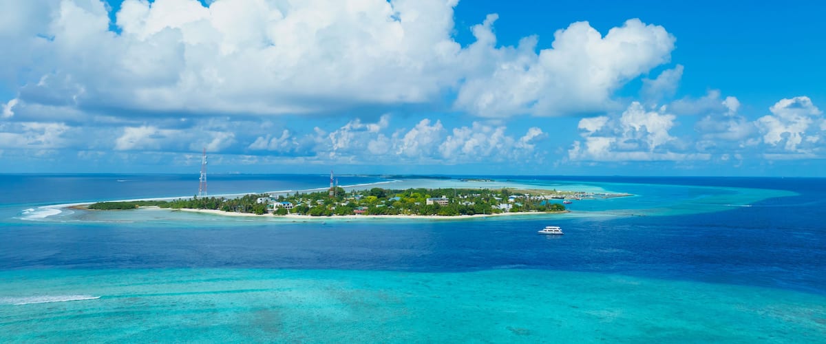 A tropical island with clear turquoise waters, a small boat, and a lighthouse.