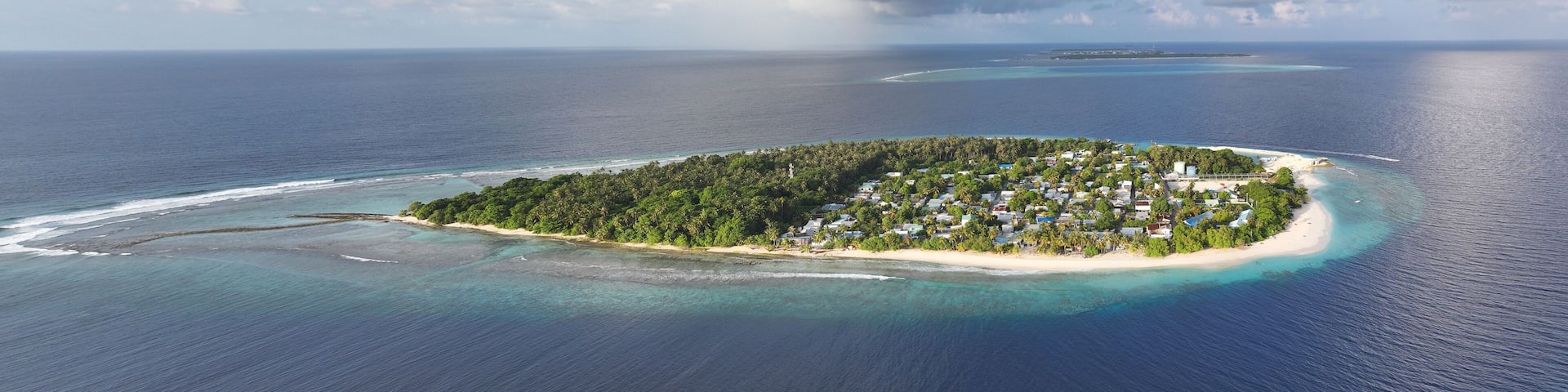 Aerial view of an island lush with green vegetation, white sandy beaches, and clusters of buildings surrounded by the deep blue sea, Maalhos, Baa Atoll, Maldives.