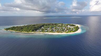 Aerial view of an island lush with green vegetation, white sandy beaches, and clusters of buildings surrounded by the deep blue sea, Maalhos, Baa Atoll, Maldives.